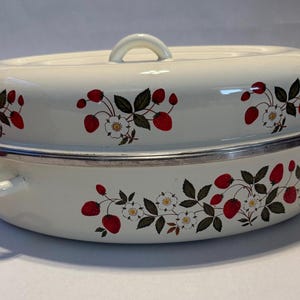 May include: Cream-colored oval enamel roaster with a matching lid. The roaster is decorated with a strawberry and floral pattern. It has a silver rim and handles for easy use.