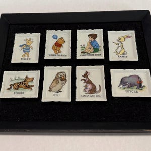 Könnte beinhalten: Ein gerahmtes Set aus acht kleinen rechteckigen Porzellanschalen, jede mit einer anderen Illustration von Winnie-the-Pooh-Charakteren. Zu den Charakteren gehören Ferkel, Winnie Puuh, Christopher Robin, Rabbit, Tiger, Eule, Kanga und Roo sowie Eeyore.