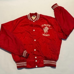 May include: A red satin jacket with white and red striped trim on the collar, cuffs, and waistband. The jacket features the embroidered text "LA FOLLETTE HOCKEY" with a horse graphic on the front.
