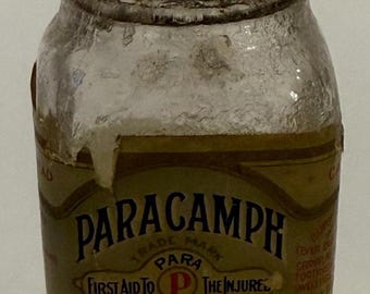 May include: A vintage glass bottle with a metal lid, labeled "PARACAMPH" with the text "First Aid To The Injured" and "Price 50 Cents". The bottle is filled with a white substance.
