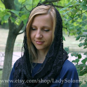 May include: A black lace head covering with a floral pattern. The lace is soft and delicate, and the head covering is worn by a person with blonde hair.