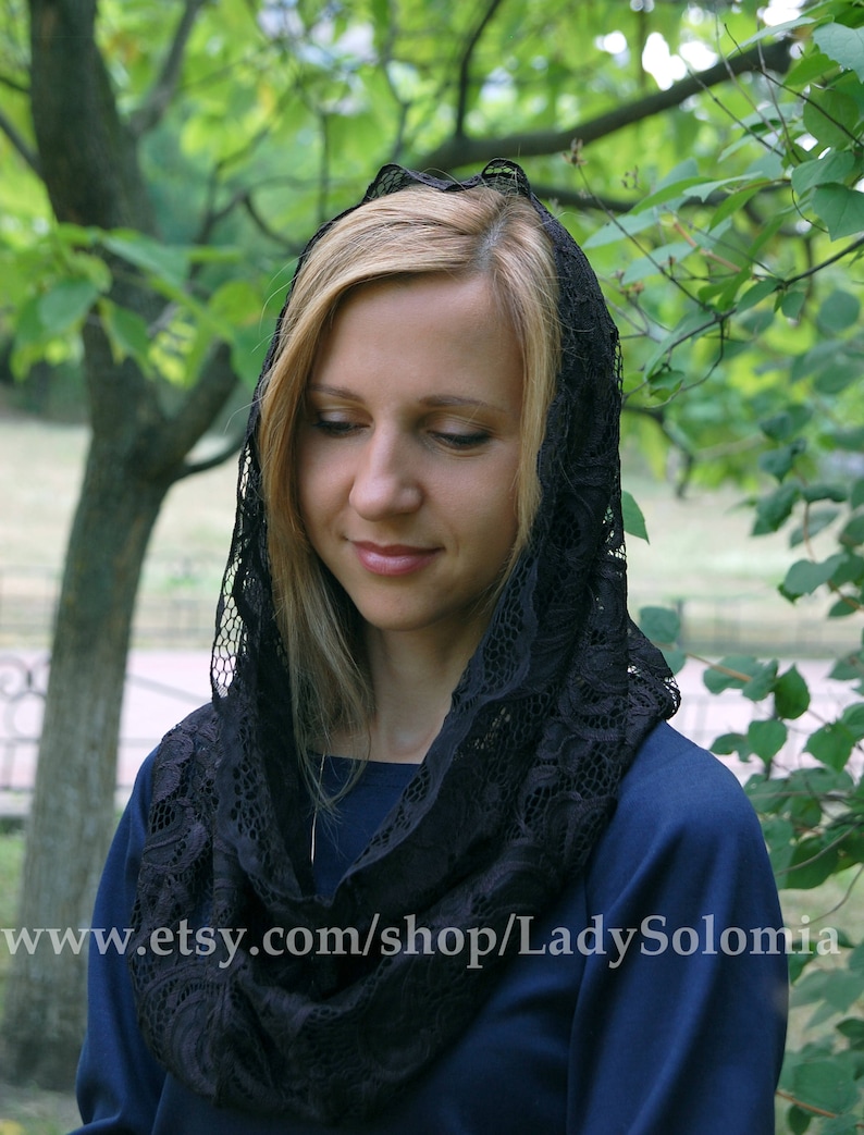May include: A black lace head covering with a floral pattern. The lace is soft and delicate, and the head covering is worn by a person with blonde hair.