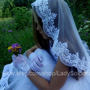 Puede incluir: Un velo blanco con intrincados bordados florales con lentejuelas y cuentas en los bordes, combinado con guantes de encaje blanco a juego que presentan un delicado patr&oacute;n floral y un borde festoneado, usado con un vestido de tul blanco.