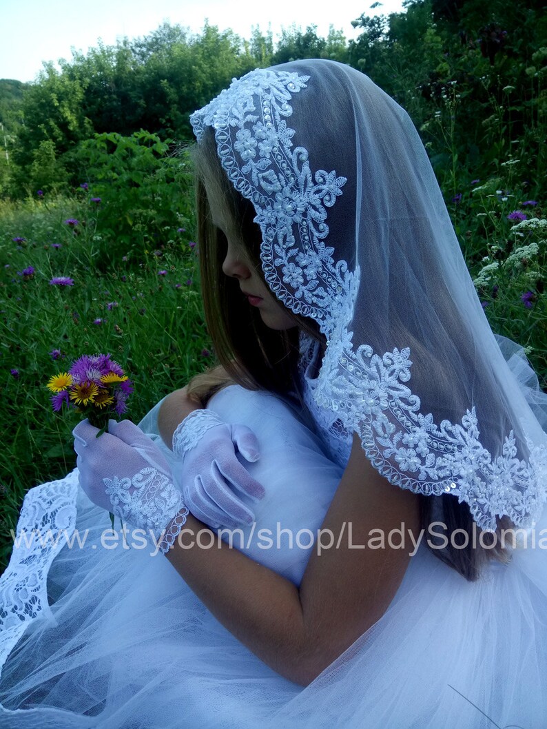 Puede incluir: Un velo blanco con intrincados bordados florales con lentejuelas y cuentas en los bordes, combinado con guantes de encaje blanco a juego que presentan un delicado patr&oacute;n floral y un borde festoneado, usado con un vestido de tul blanco.