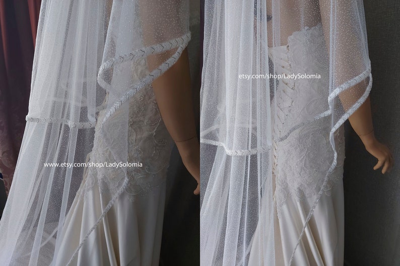 Puede incluir: Un velo de novia blanco con un acabado brillante sutil y un borde trenzado decorativo, combinado con un vestido largo con detalles de encaje aplicado, una espalda estilo cors&eacute; con cordones y una falda de sat&eacute;n suave. El texto dice etsy.com/shop/LadySolomia.