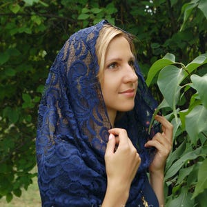 May include: A navy blue lace head covering with a floral pattern. The lace is delicate and intricate. The head covering is worn by a person with blonde hair.
