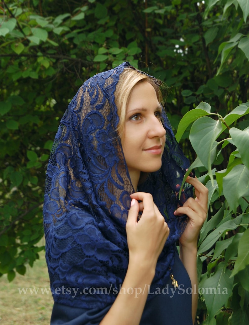 May include: A navy blue lace head covering with a floral pattern. The lace is delicate and intricate. The head covering is worn by a person with blonde hair.