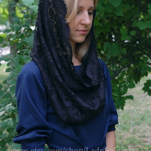 May include: A black lace head covering with a floral pattern. The lace is draped over a woman's head and shoulders. She is wearing a dark blue dress.