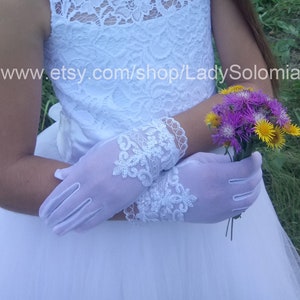 Puede incluir: Guantes blancos hasta la mu&ntilde;eca con intrincados bordados de encaje floral y bordes festoneados en los pu&ntilde;os. Los guantes se llevan con un vestido blanco con estampado de encaje y sostienen un peque&ntilde;o ramo de flores silvestres moradas y amarillas. El texto dice www.etsy.com/shop/LadySolomia.