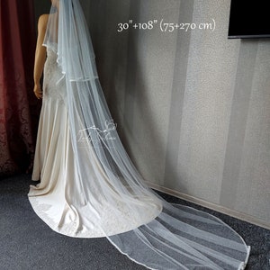 Puede incluir: Un velo de novia blanco de dos niveles hecho de tela de tul transparente. El velo presenta una capa superior m&aacute;s corta de 75 cm y una capa inferior m&aacute;s larga de 270 cm. Los bordes tienen un acabado con un ribete delicado sobre un vestido.