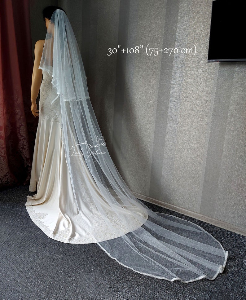 Puede incluir: Un velo de novia blanco de dos niveles hecho de tela de tul transparente. El velo presenta una capa superior m&aacute;s corta de 75 cm y una capa inferior m&aacute;s larga de 270 cm. Los bordes tienen un acabado con un ribete delicado sobre un vestido.