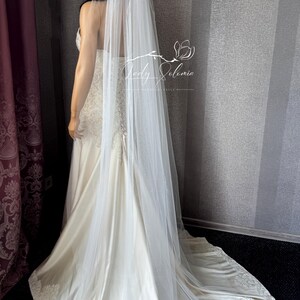May include: A long, sheer white wedding veil measuring 80 inches in length, draped over a floor-length ivory gown with lace detailing at the hem. The veil is made of fine, translucent tulle fabric and features a simple, unadorned edge design.