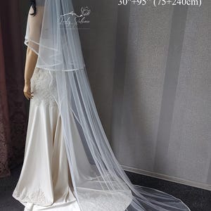 Puede incluir: Un velo de novia blanco de dos niveles con un delicado borde de cuentas, que presenta una capa m&aacute;s corta de 75 cm y una cola m&aacute;s larga de 240 cm. La tela de tul transparente cae con elegancia, mostrando un detalle refinado en el borde.