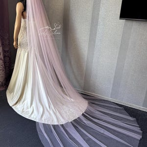 May include: A long, pale pink tulle wedding veil measuring 108 inches in length. The veil is draped over a mannequin wearing a white satin gown with lace detailing at the hem. The text 108" (270 cm) is visible in the upper center of the image.