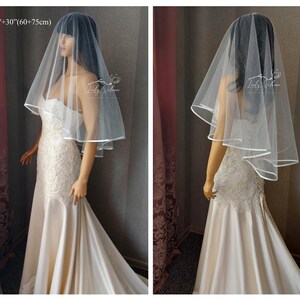 May include: A white bridal veil with a single layer of tulle and a satin edge. The veil is 24 inches long and has a 30 inch drop. The veil is shown on a model wearing a white wedding dress.