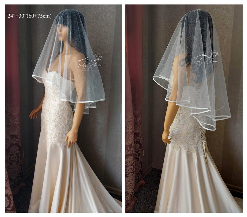 May include: A white bridal veil with a single layer of tulle and a satin edge. The veil is 24 inches long and has a 30 inch drop. The veil is shown on a model wearing a white wedding dress.