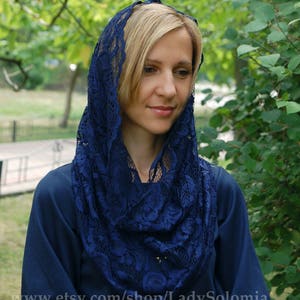 May include: A woman wearing a navy blue lace shawl over a dark blue dress. The shawl is made of delicate lace with a floral pattern.