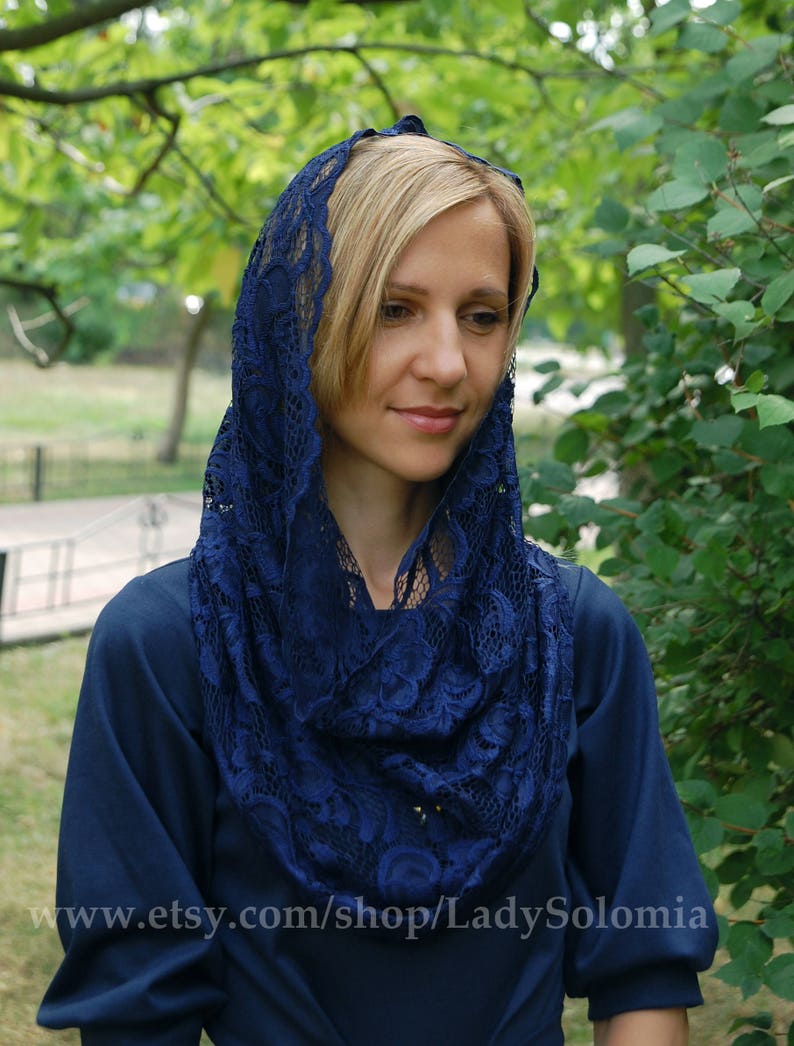 May include: A woman wearing a navy blue lace shawl over a dark blue dress. The shawl is made of delicate lace with a floral pattern.