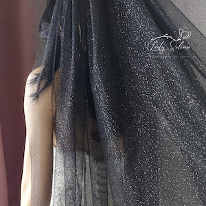 May include: Black tulle veil with silver glitter dots. The veil is sheer and has a delicate, flowing texture.