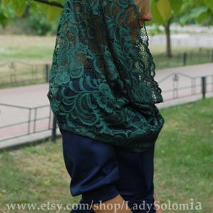 May include: A dark green lace mantilla with a floral pattern. The mantilla is draped over a person's head and shoulders.