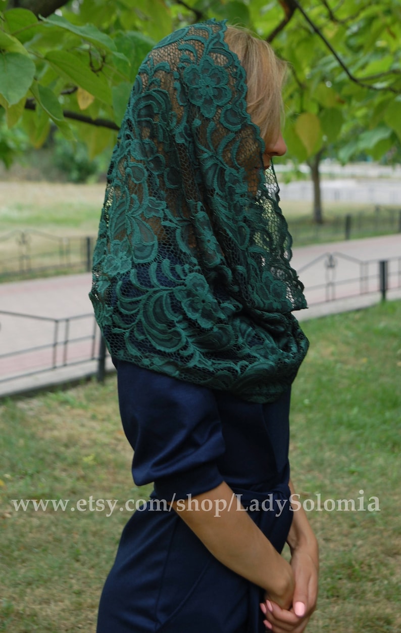May include: A dark green lace mantilla with a floral pattern. The mantilla is draped over a person's head and shoulders.