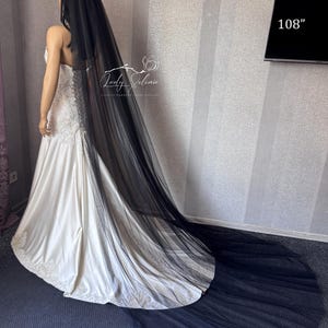 May include: A long black tulle wedding veil measuring 108 inches in length, draped over a white satin wedding dress with lace detailing at the hem. The veil is sheer, floor-length, and extends beyond the train of the dress on the floor.