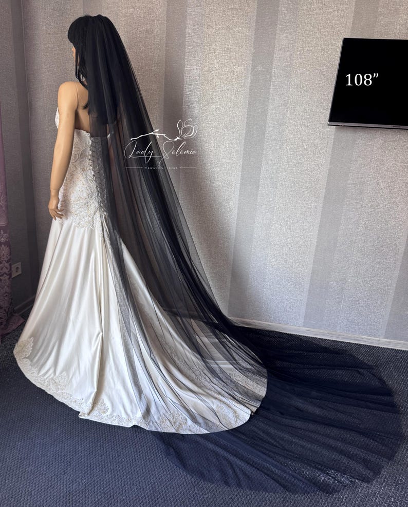 May include: A long black tulle wedding veil measuring 108 inches in length, draped over a white satin wedding dress with lace detailing at the hem. The veil is sheer, floor-length, and extends beyond the train of the dress on the floor.
