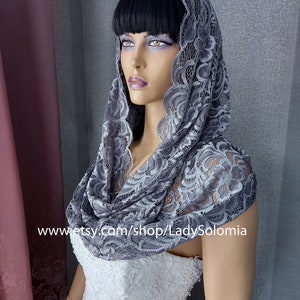 May include: A gray lace shawl with a floral pattern. The shawl is draped over a mannequin's shoulders and head. The mannequin is wearing a white dress.