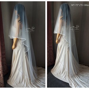 May include: A white bridal veil with a satin edge. The veil is 30 inches long and has a 72 inch train. The veil is shown on a mannequin wearing a white wedding dress.