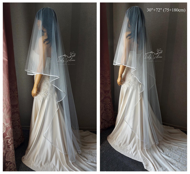 May include: A white bridal veil with a satin edge. The veil is 30 inches long and has a 72 inch train. The veil is shown on a mannequin wearing a white wedding dress.