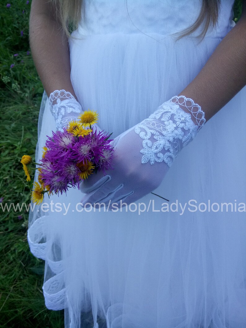 Puede incluir: Guantes blancos transparentes hasta la mu&ntilde;eca con intrincados bordados de encaje floral y borde festoneado. Los guantes se llevan con un vestido de tul blanco y sostienen un peque&ntilde;o ramo de flores silvestres moradas y amarillas. Texto: www.etsy.com/shop/LadySolomia.
