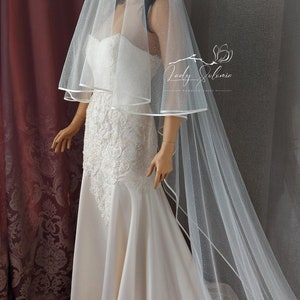 May include: A white bridal veil with a delicate sparkle and a satin trim. The veil is layered and has a long, flowing train.