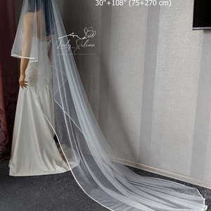 May include: A white bridal veil with a sparkling design and a white satin trim. The veil is 30 inches long and has a 108-inch train, for a total length of 138 inches.