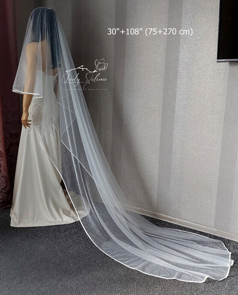 May include: A white bridal veil with a sparkling design and a white satin trim. The veil is 30 inches long and has a 108-inch train, for a total length of 138 inches.