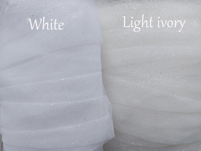Puede incluir: Dos rollos de tela de tul transparente con purpurina mostrados uno al lado del otro. El rollo izquierdo est&aacute; etiquetado como White y el derecho como Light ivory. Ambas telas presentan una textura de malla fina y transl&uacute;cida con destellos.