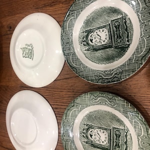 May include: Two white saucers and two green and white plates with a clock design. The plates have a green border with a repeating pattern. The clock design is in the center of the plate.