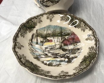 Può includere: Servizio da tè color crema con una scena di paesaggio invernale con edifici dai tetti rossi, alberi e un fiume innevato. Il set ha un bordo floreale marrone decorativo.