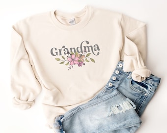 May include: A cream-colored sweatshirt with the word "Grandma" in a gray script font and a floral design with pink flowers and green leaves.