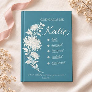 May include: A teal hardcover journal featuring a white floral illustration on the left side. The text reads: GOD CALLS ME Katie, kept Jude 1:24, accepted Ephesians 1:6, treasured Titus 2:14, included Ephesians 1:13, empowered Acts 1:8, and Isaiah 43:1.