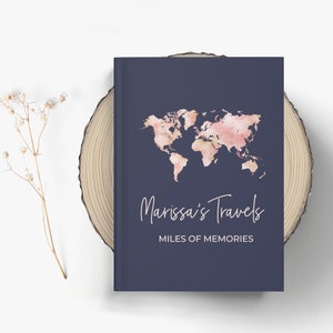 May include: A navy blue travel journal with a pink and gold watercolor world map and the text "Marissa's Travels" and "Miles of Memories".