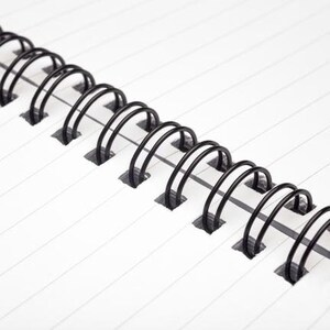 May include: Close-up of a black wire binding on a notebook. The binding is made of metal and has a series of loops that hold the pages together.