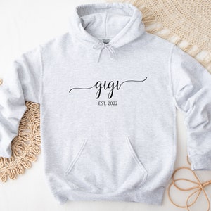 May include: Gray hooded sweatshirt with the text "gigi est. 2022" in black cursive lettering.