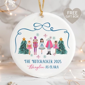 May include: White ceramic Christmas ornament featuring a watercolor illustration of characters from The Nutcracker ballet. The ornament includes text that reads "The Nutcracker 2025" and "Braylee as Clara". A gold ribbon is attached for hanging.
