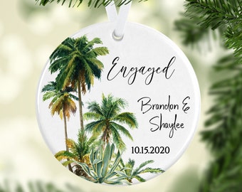 May include: White round bauble with a tropical palm tree design. The bauble says "Engaged" with the names "Brandon & Shaylee" and the date "10.15.2020".