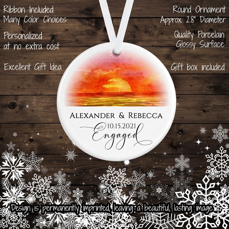 May include: A white round porcelain ornament with a watercolor sunset scene and the text "ALEXANDER & REBECCA 10.15.2021 Engaged". The ornament is 2.8 inches in diameter and comes with a ribbon and gift box.