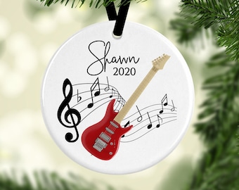 May include: White round Christmas ornament with a red electric guitar, musical notes, and the name "Shawn 2020" in black script.