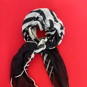 Puede incluir: Bufanda de gasa a rayas blancas y negras con un borde blanco. La bufanda está doblada y anudada. La marca "ECRU" es visible en la bufanda.
