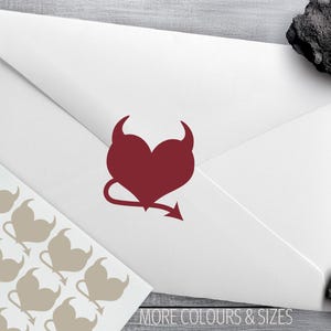 May include: A white envelope with a burgundy heart-shaped devil design and a sheet of stickers with the same design. The text "MORE COLOURS & SIZES" is at the bottom. The logo "Confetti Barn" is in the top left corner.