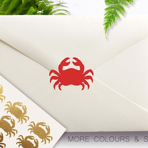 May include: A sheet of gold foil stickers with a crab design. The stickers are arranged in a grid pattern. There is a red crab sticker on a white envelope. The text "MORE COLOURS & SIZES" is at the bottom of the image.