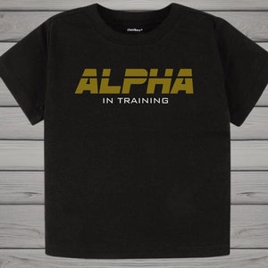 May include: Black t-shirt with the text "ALPHA IN TRAINING" in gold lettering. The shirt is a basic crew neck style, suitable for casual wear. The brand name "Gerber" is visible on the neckline.